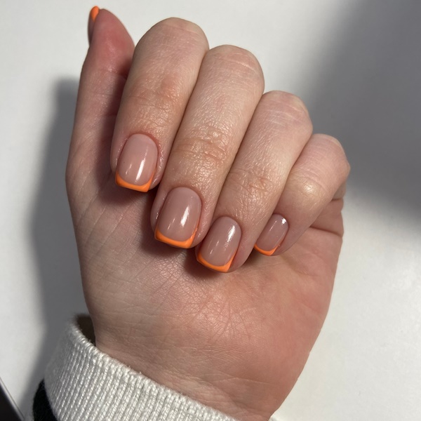 mulher com unhas francesinhas na cor nude e ponta laranja